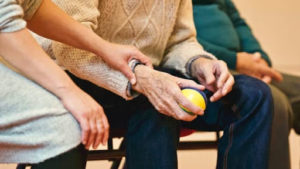 An elderly person holds a ball while sitting next to a young woman