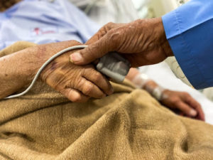An elderly patient holds hands with their care provider